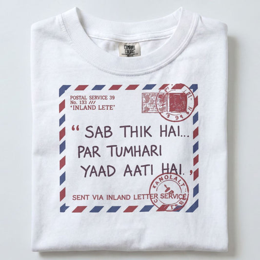 A folded white t-shirt featuring a printed graphic of a vintage airmail letter with Hindi text and red postage stamps.