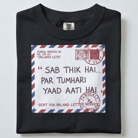 A folded black t-shirt with a graphic print of a vintage Indian postal letter envelope. The graphic features a red and blue striped border, a red stamp, and Hindi text that reads 'Sab thik hai.